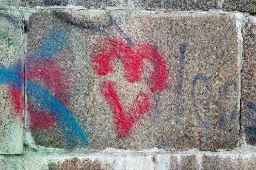 Red heart painted on ancient stone block wall background.