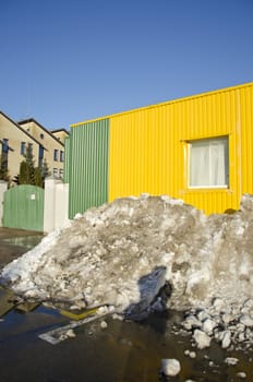 pile of melting snow in spring near industrial building.