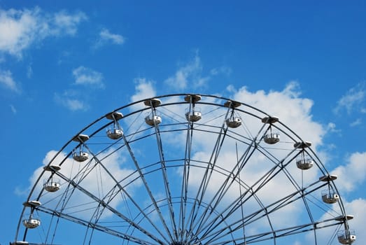 Half Ferris wheel on blue sky and white clouds