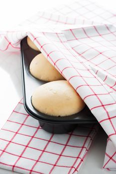 Yeast dough in a muffin pan with a white and red towel on white background as a studio shot