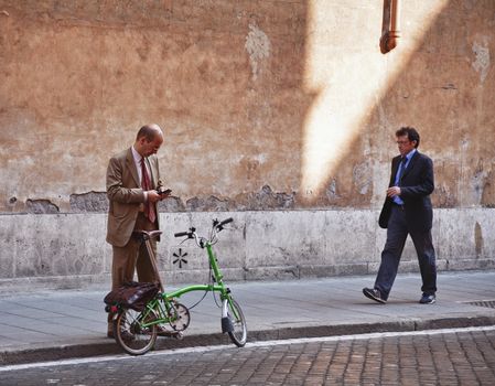 BUSINESSMEN ON THE MOVE, ROME, ITALY, SEPTEMBER 29, 2011: Mature man checking his mobile in the street at lunch time while another man is walking by.