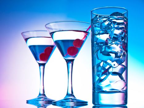 Two glasses of martini with red cherries and a glass of clear cocktail