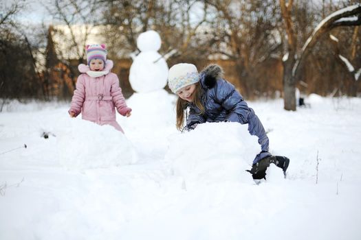 Two sisters rolling snow to make snowman