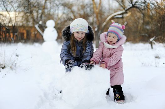 Two sisters rolling snow to make snowman