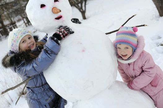 An portraits of happy sisters posing with snowman