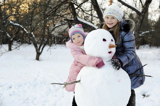 An image of happy sisters posing with snowman