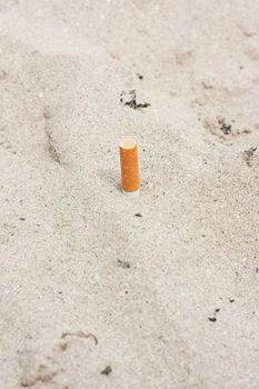 A cigarette butt crushed in the sand illustrating pollution by man