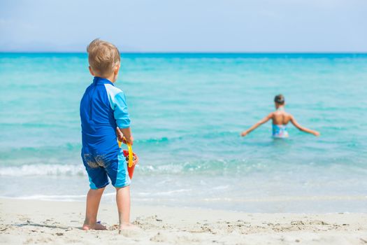 Back view young boy on sandy tropical beach, his sister background.