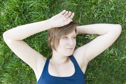 Attractive girl in blue shirt is resting on the grass. 
