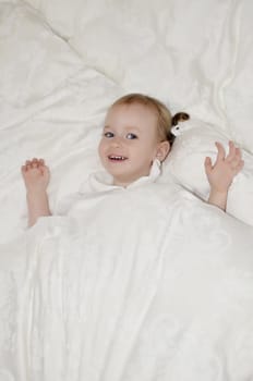 Funny little girl lying on the bed under the covers.