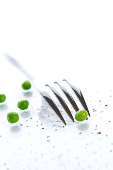 Fork has put teeth into a pea. Salt and pepper sprinkled over
