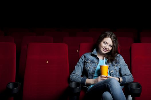 beautiful woman in a movie theater, watching a movie and drink a drink