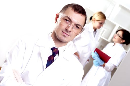 Three doctors are smiling at the camera in a doctors' office. Horizontally framed shot.