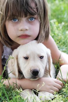 A little girl and her puppy, Cloud, an English Cream Labrador Retriever - Golden Retriever mixed designer breed 7 week old puppy,  resting after playing together. Extreme shallow depth of field with selective focus on on child's and puppies faces.