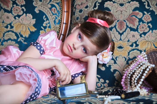 A girl plays with her ​​mother's jewelry lying on the couch.