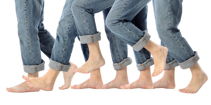 A womans bare feet advance one step forward in rolled up jeans on white