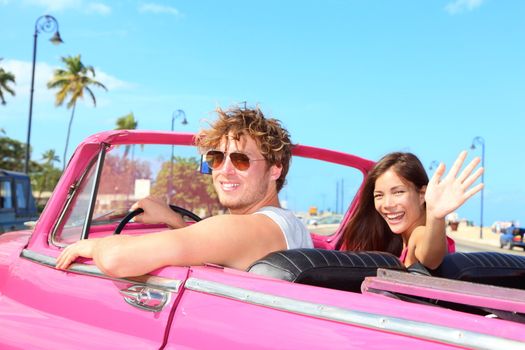 Couple happy in vintage retro convertible car. Friends driving on summer road trip in pink car. Beautiful young Caucasian man and Asian woman model smiling joyful on sunny summer day travelin Havana, Cuba.