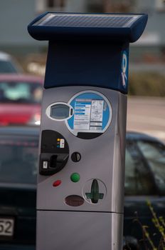 Modern solar powered pay parking machine with cars in the background