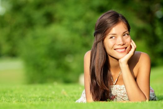 Asian woman lying in grass smiling happy looking at copy space. Beautiful girl in spring / summer relaxing and thinking. Mixed race Caucasian / Asian Chinese model outdoors.