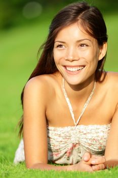 Happy asian spring woman lying in grass smiling beautiful in summer dress. Pretty mixed race Asian / Caucasian girl.