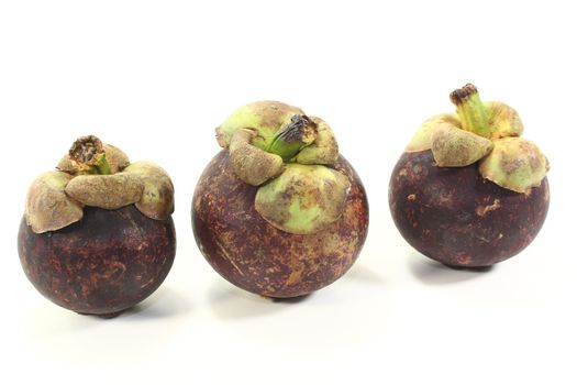 three fresh mangosteen fruits on a light background