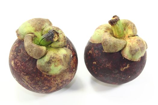 two fresh mangosteen fruits on a light background