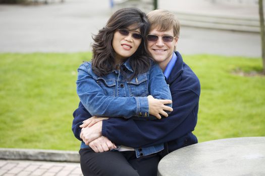 Beautiful Caucasian, Asian couple sitting outdoors together, hugging.