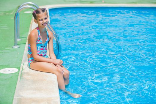 Pretty young girl sit at pool's edge