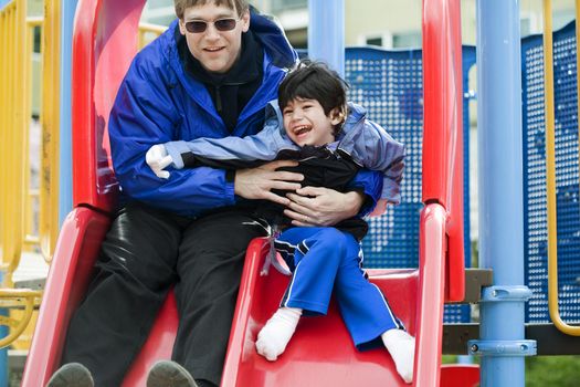 Father going down slide with disabled son who has cerebral palsy