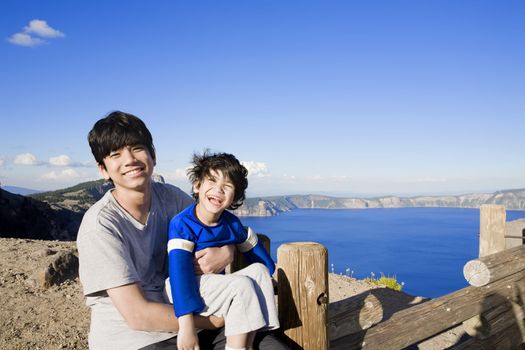 Big brother holding smiling disabled little boy with Oregon's famous Crater Lake in the bakcground. Child has cerebral palsy