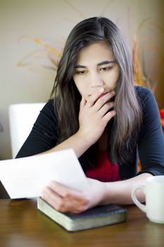 Biracial teenage girl or young woman reading  note in hand with worried or sad expression