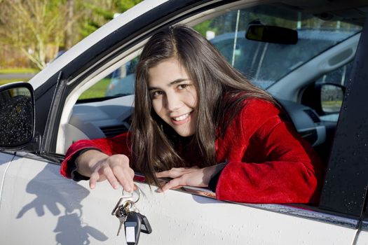 Beautiful biracial teenage girl in driver's seat holding keys to white car