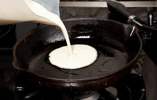 Frying pan on gas stove with pancake mixture being cooked
