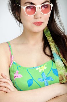 Cropped head and shoulders portrait of an attractive sexy woman in rose coloured sunglasses and a green summer dress standing with folded arms looking at the camera