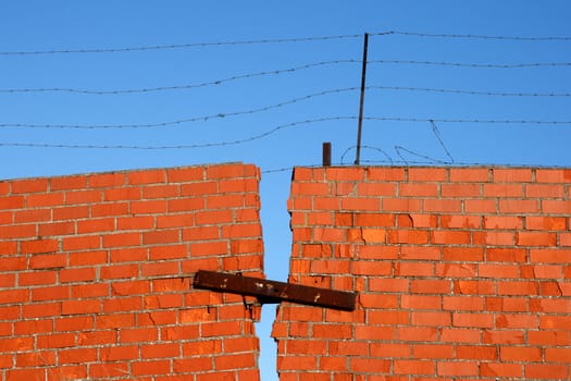 Red Brick broken Wall with barbed wire against blue sky