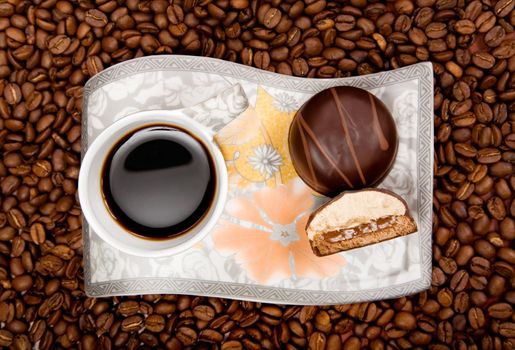 Coffee cup with sweets on beans background, high angle view 