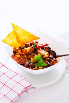 Chili con carne in a white bowl with two chips on white background a as studio shot