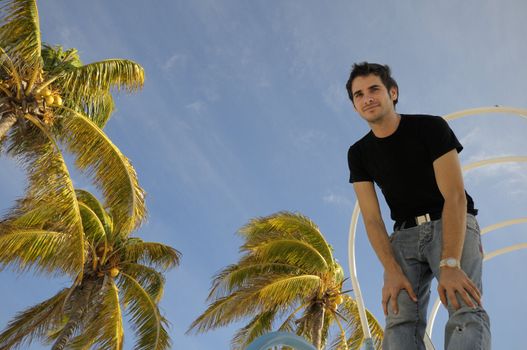 Young man standing against tropical sky background with coconut palm trees