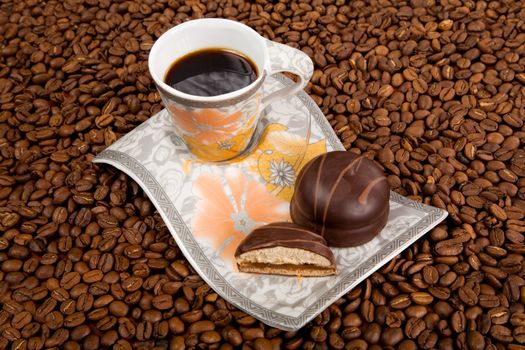 Coffee cup with sweets on beans background 