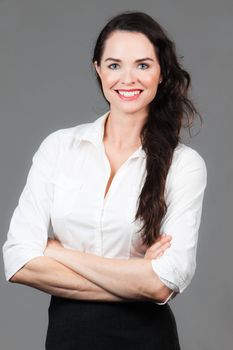 Portrait of a happy young business woman with arms folded, over grey background