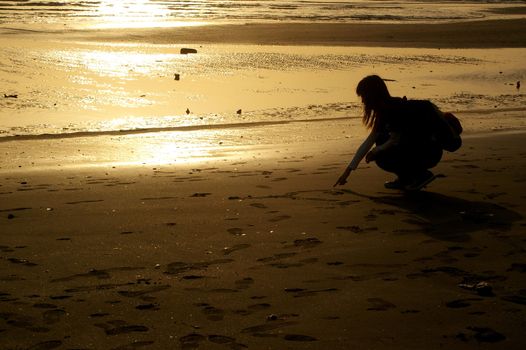 Girl drawing on sand at sunset