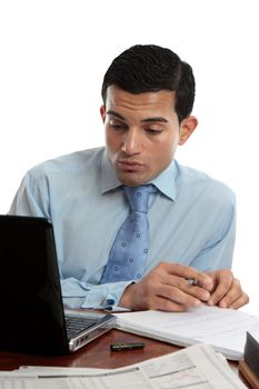 A businessman sitting at desk with paperwork, laptop and notebook working hard.