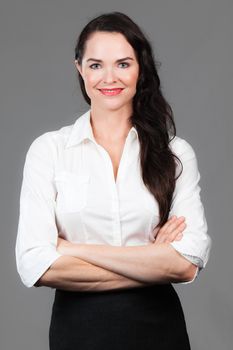 Portrait of a happy young business woman with arms folded, over grey background