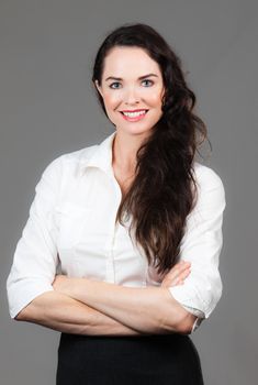 Portrait of a happy young business woman with arms folded, over grey background