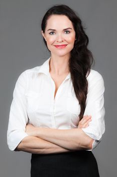 Portrait of a beautiful young business woman with arms folded, over grey background