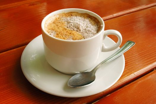 Cappuccino cup with metal spoon on wood background