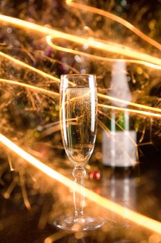 New Year card with champagne glass and sparkles, blurred bottle on background 