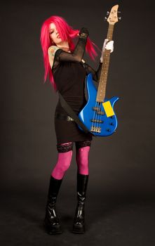 Attractive girl putting on bass guitar, studio shot on black background 