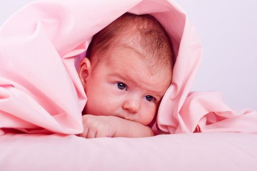 View of a newborn baby on a smooth bed hidden on the sheet.