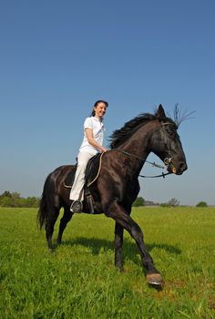 young woman and her black stallion in a field in spring